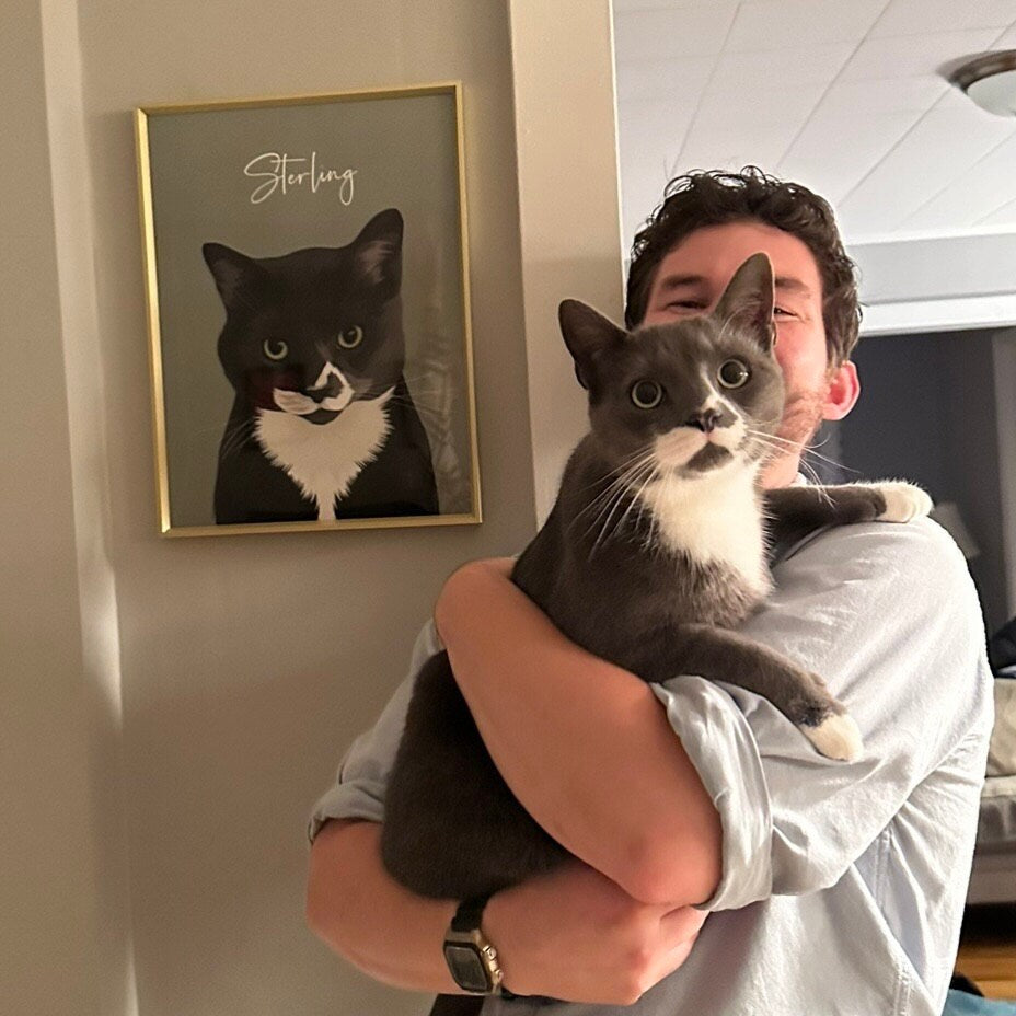 Sterling the cat held beside their framed custom Print & Paw portrait